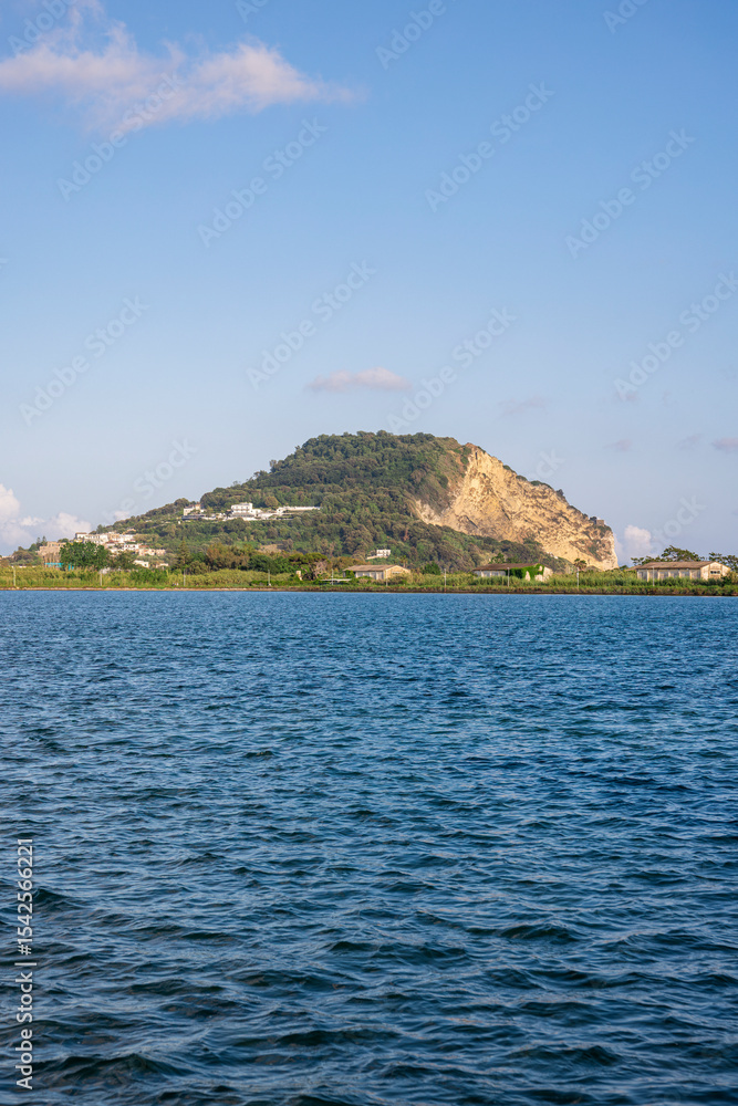 Fototapeta premium A tranquil view of Capo Miseno in Bacoli, Italy, seen from the calm blue waters under a bright summer sky