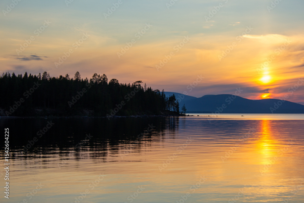 Obraz premium Beautiful lake sunset with golden reflections on calm water, forest silhouette, and soft mountain horizon. Peaceful twilight scene ideal for nature, travel, background, and relaxation concepts.
