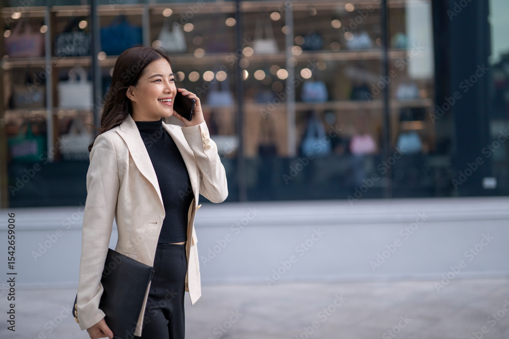 Fototapeta premium Smiling businesswoman walking and talking on phone in urban setting