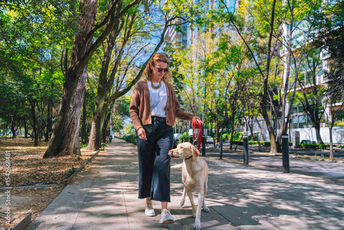 A woman is walking her dog along a tree-lined path in Mexico City’s Polanco neighborhood, surrounded by greenery and urban buildings in the background.