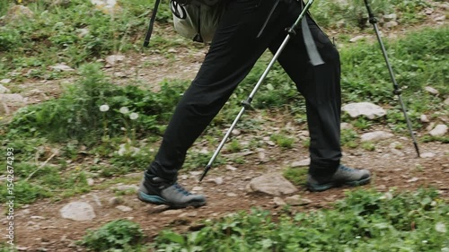 Close up of hiker legs walking on mountain trail with trekking poles.