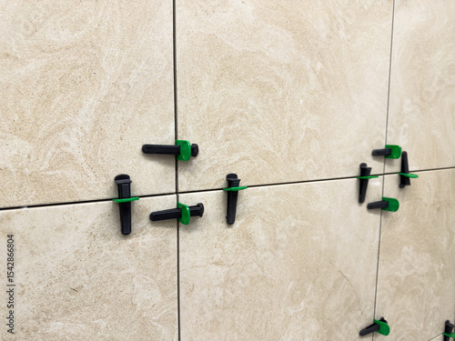 Beige marble style ceramic tiles installed with leveling system. Close up shows neat grout lines and surface alignment during precise wall finishing in interior remodeling