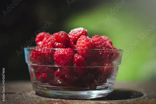 Transparent plate with juicy sweet raspberries on wooden table