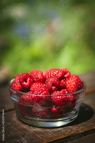 Transparent plate with juicy sweet raspberries on wooden table