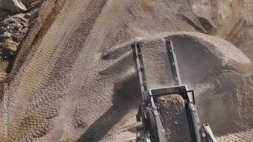 Top-down aerial view of a rock crusher's conveyor belts dropping processed gravel onto a large stockpile at a mining quarry. Industrial production of construction materials.
