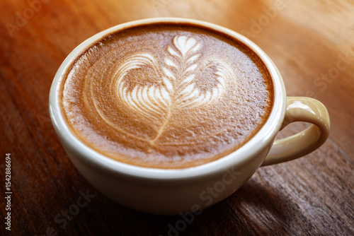 Rosetta pattern latte art in ceramic coffee cup on  wooden table , flat lay with copy space , warm tones