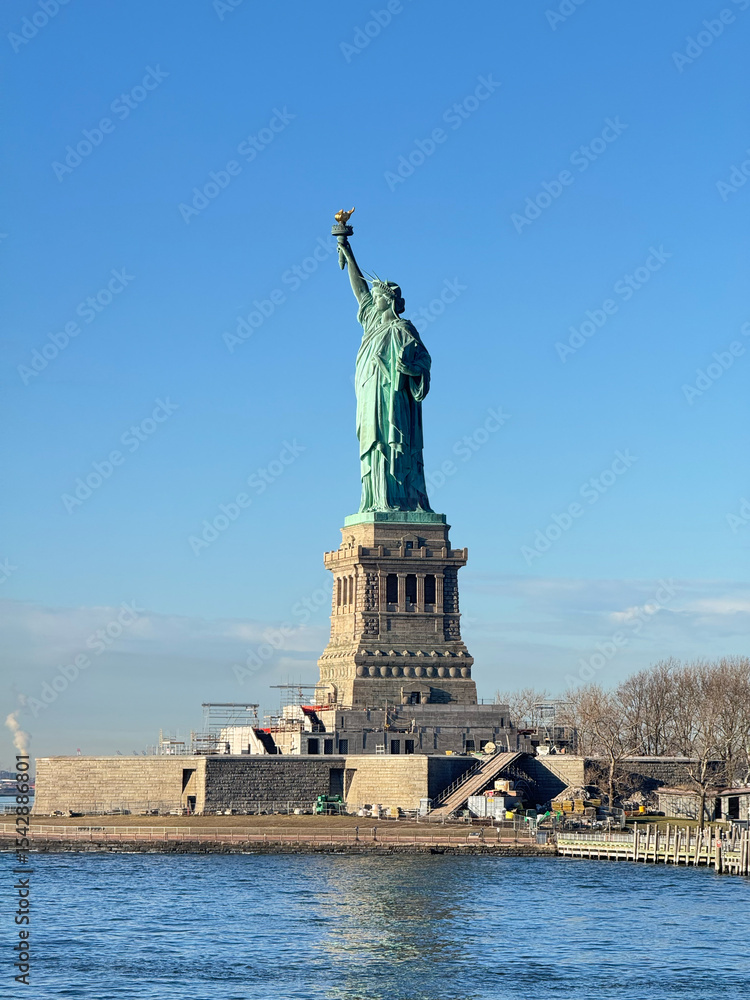 Fototapeta premium The Statue of Liberty, a symbol of New York. The goddess statue is looking left.Vertical. There is construction going on under the pedestal. From the ferry to Liberty Island.