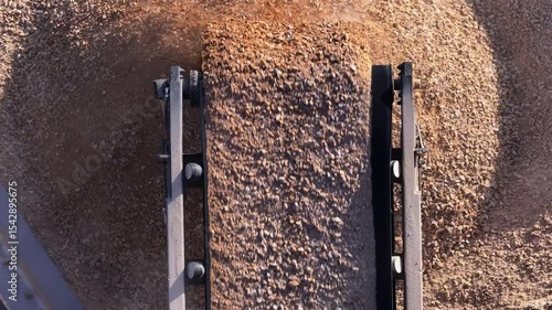 Top-down aerial view of a conveyor belt dropping crushed stone onto a large pile. Industrial machinery at a gravel pit or mining quarry for producing construction materials.
