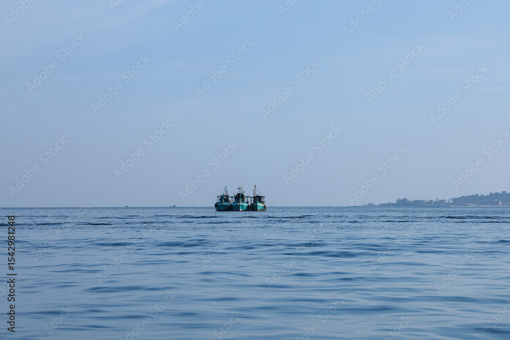 Obraz premium Three fishing boats at sea under a calm blue sky