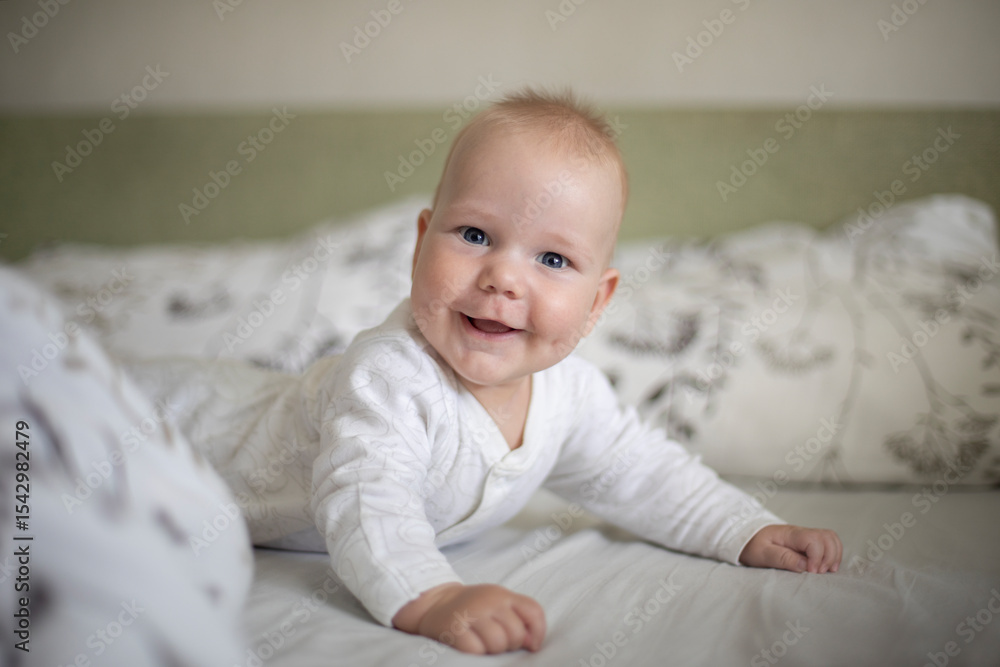 4 month old baby lying on his stomach on the bed, dressed in light clothes, joy and smile on his face
4 month old baby lying on his stomach on the bed, dressed in light clothes, joy and smile on his face