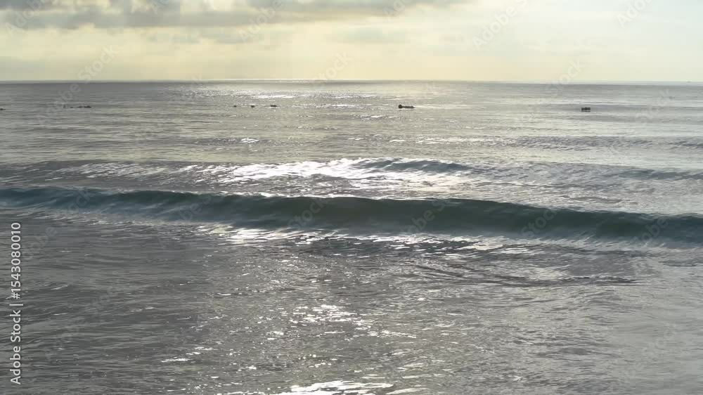 Morning waves rolling gently onto the shore on a cloudy day, as seen from the coast of Bali, Indonesia Morning waves rolling gently onto the shore on a cloudy day, as seen from the coast of Bali, Indonesia