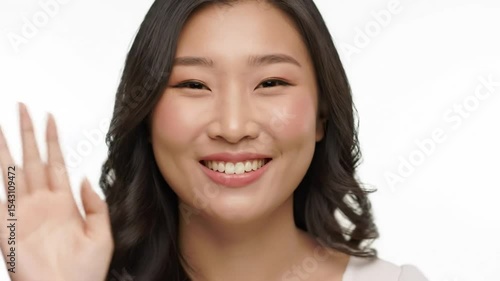 Hello, welcome. Portrait of happy young woman appear at the video waving hi with her palm, greeting with hospitable friendly smile Indoor studio shot isolated on white background 