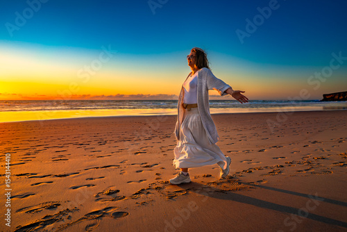 Beautiful middle-aged woman enjoying walk on sandy beach on sunset on windy spring day. Side view. Monte Clerigo beach on Algarve coast in Portugal