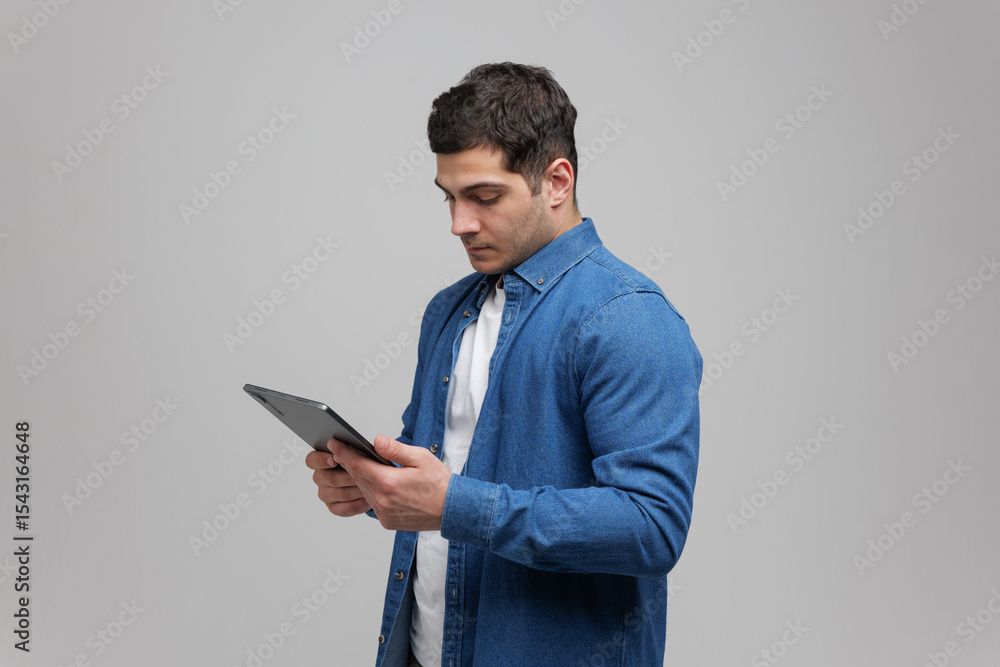 Focused Young Man Interacts With a Tablet, Showcasing Modern Technology in a Minimalist Studio Setting Focused Young Man Interacts With a Tablet, Showcasing Modern Technology in a Minimalist Studio Setting