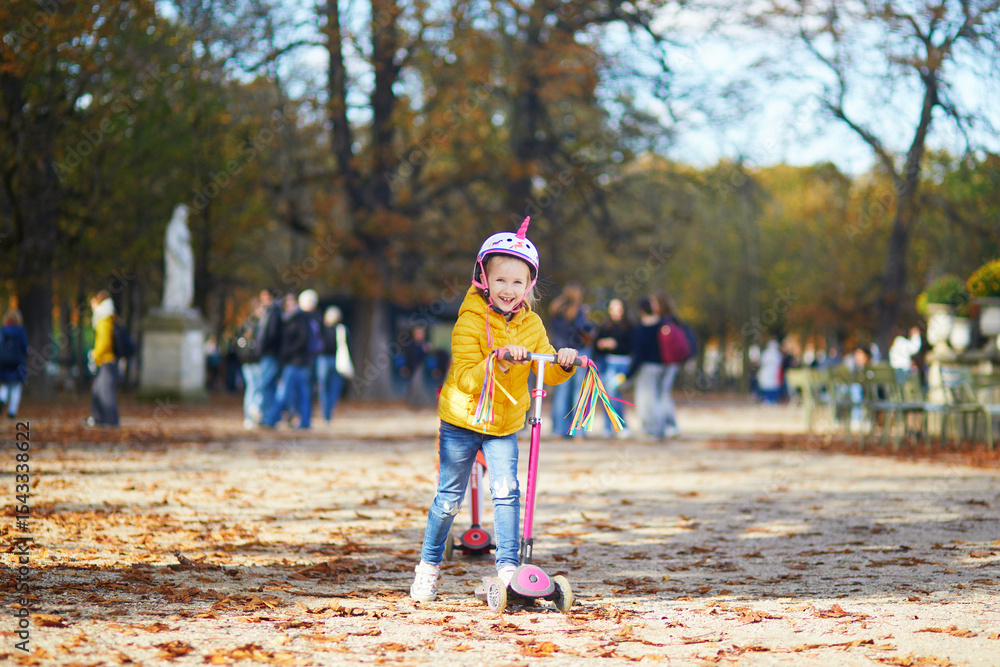Fototapeta premium Cheerful little girl enjoying her walk in autumn park in Paris, France.
