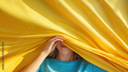 A woman playfully peeks from behind a bright yellow curtain, creating a joyful and vibrant atmosphere that captures the essence of warmth and delight in life.