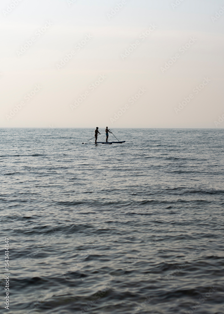 Fototapeta premium Two people paddleboarding on calm water during a serene day. The scene captures a peaceful outdoor activity in nature.