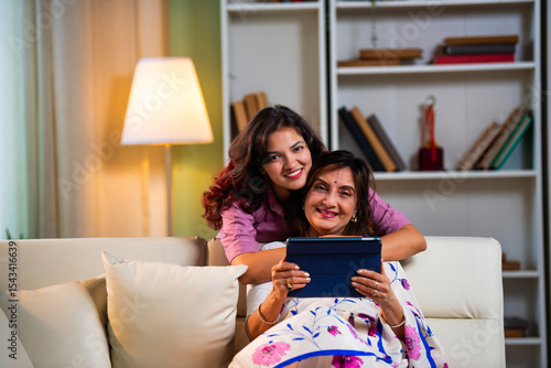 Canvas Print Indian mother and daughter browsing internet happily on tablet while seated in l