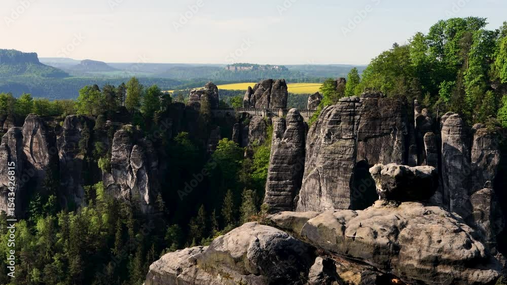 Scenic view of famous Bastai Bridge sprawling over cliffs in Saxon Switzerland National Park, Germany. Yellow rapeseed field can be seen in distance. Travel, European attractions Scenic view of famous Bastai Bridge sprawling over cliffs in Saxon Switzerland National Park, Germany. Yellow rapeseed field can be seen in distance. Travel, European attractions
