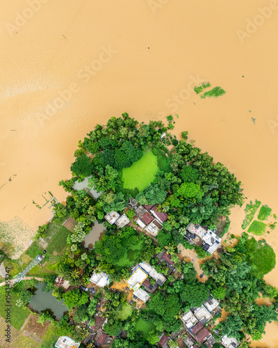 Aerial view of flooded village with muddy brown water submerging homes and roads after heavy rainfall.