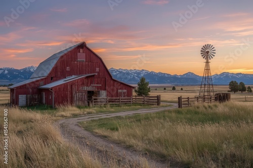 Red barn silhouetted against a vibrant sunset with a windmill in the scene.


