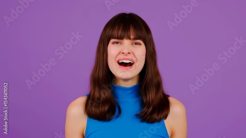 Expressive brunette in a blue top looks at the camera, making goofy faces by puffing her cheeks and making fish lips, then bursts into a joyful laugh.