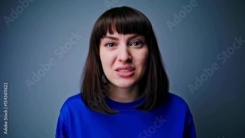 Medium close-up of a fun-loving woman in a blue sweatshirt making various expressions, from a big toothy smile to puckered lips and playful hand gestures around her eyes in a studio.