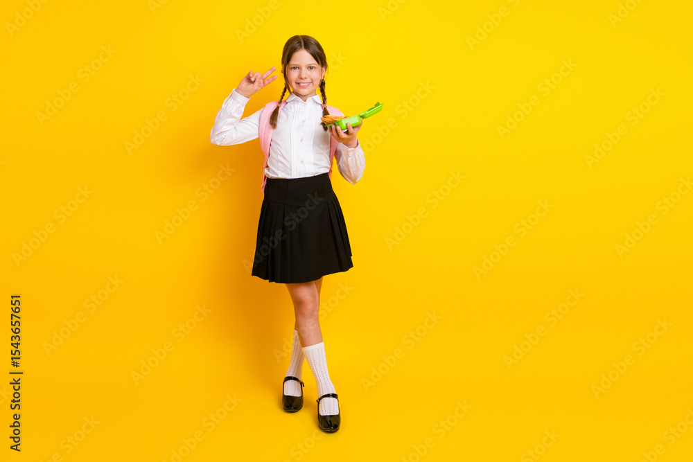 Cheerful schoolgirl holding a green exercise book, smiling against a vibrant yellow background Cheerful schoolgirl holding a green exercise book, smiling against a vibrant yellow background