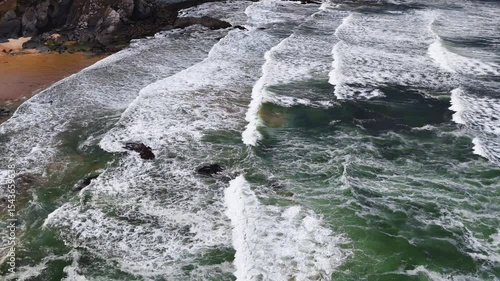 Moving aerial view following ocean waves as they roll and crash along the shore at Praia da Amália, Costa Vicentina, Portugal. Showcasing the energy and flow of the coastal scene.