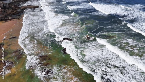 Moving aerial view following ocean waves as they roll and crash along the shore at Praia da Amália, Costa Vicentina, Portugal. Showcasing the energy and flow of the coastal scene.