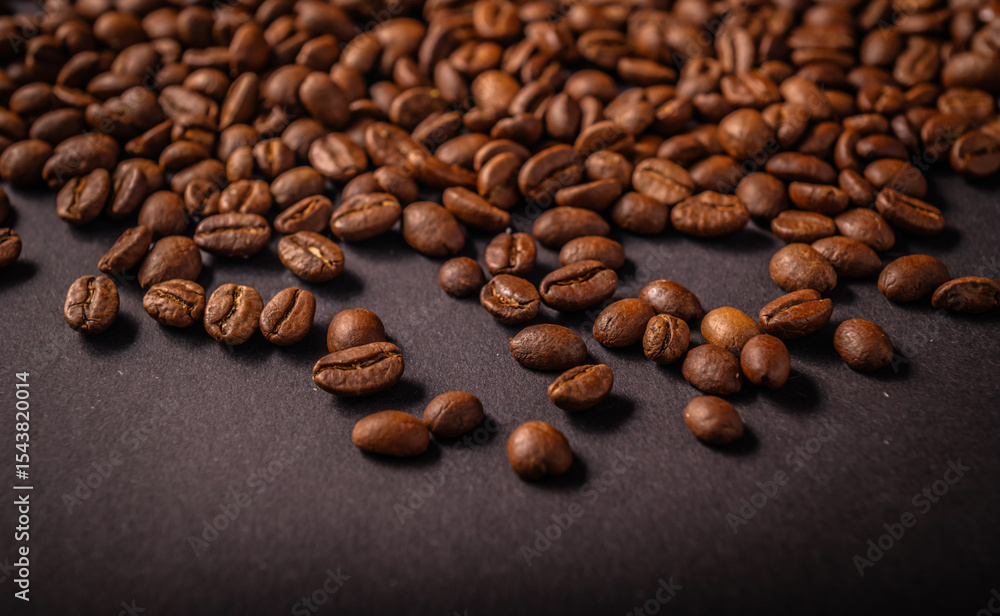 Naklejka premium Freshly roasted coffee beans lie scattered across a dark background, highlighting their glossy texture and deep brown color