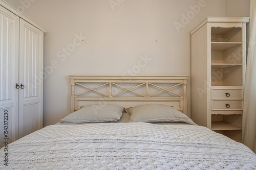 Wallpaper Mural cozy bedroom features a bed with a white crocheted blanket, matching pillows, and a decorative headboard, flanked by a wardrobe and open shelves Torontodigital.ca