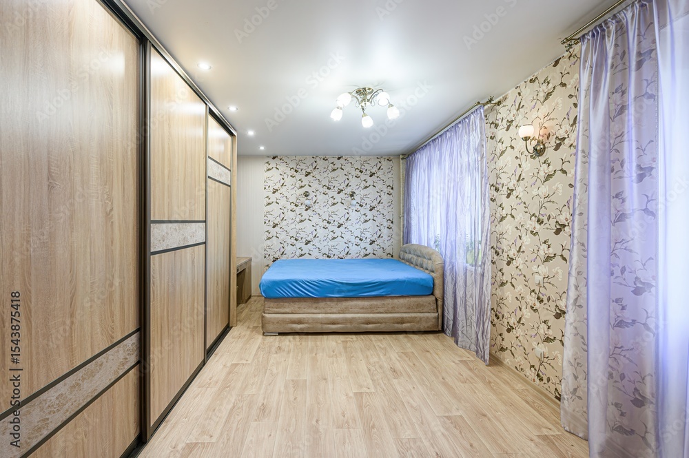 cozy bedroom features a large wooden wardrobe, a bed with a blue sheet, patterned wallpaper, and soft violet curtains cozy bedroom features a large wooden wardrobe, a bed with a blue sheet, patterned wallpaper, and soft violet curtains