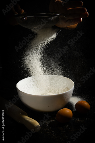 Tamizado de harina en cuenco blanco con huevos y rodillo en fondo negro