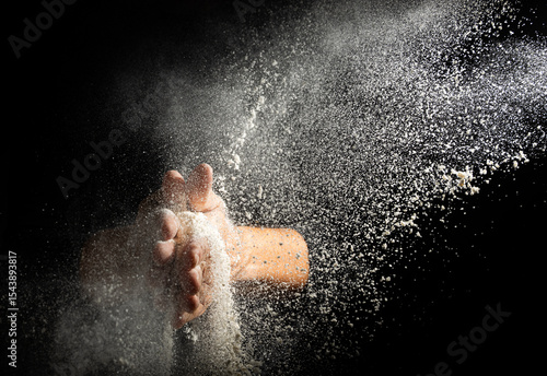 Manos espolvoreando harina con fondo negro en cocina artesanal