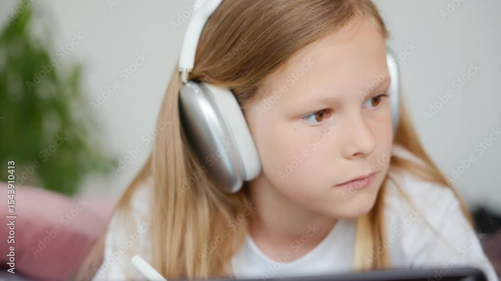 Front view of a girl with silver headphones drawing on a black tablet using a stylus. Camera slowly zooms in and out as she stays focused. White clothes, soft daylight. High quality 4k footage Front view of a girl with silver headphones drawing on a black tablet using a stylus. Camera slowly zooms in and out as she stays focused. White clothes, soft daylight. High quality 4k footage