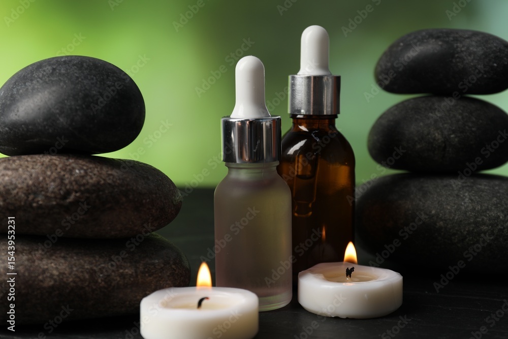 Spa composition with stones, droppers and burning candles on dark table against blurred green background, closeup Spa composition with stones, droppers and burning candles on dark table against blurred green background, closeup