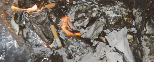 Close-up of burning household waste, showing a small flame, melting plastic, and ash. Represents illegal open burning, pollution, and bad waste management. Ideal for eco-content