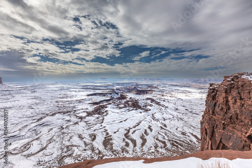 A light snowfall and contrasting orange-colored terrain define the rugged lan...