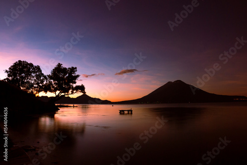 Starry night over Lake Atitlán, Guatemala. Long exposure captures stars, volcanoes and colorful village lights reflecting on calm water, evoking peace, wonder, and adventure under the vast sky.