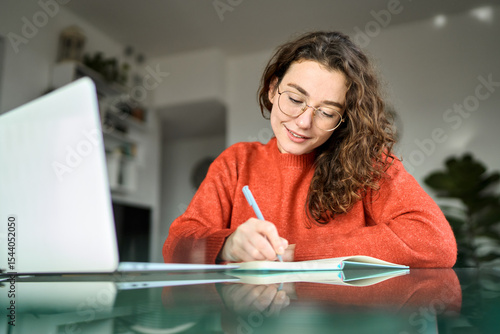 Fototapete Pretty young woman student using laptop elearning or remote working at home office using laptop computer watching webinar, learning web course, studying online sitting at table, writing notes