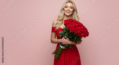 Fototapeta Naklejka Na Ścianę i Meble -  A smiling blonde woman in a red dress holding a large bouquet of red roses against a pink background