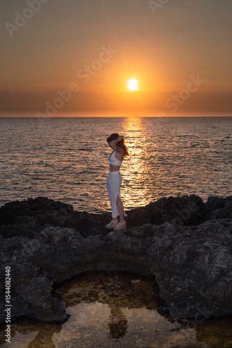 A fit girl styles her hair as sunset over the Mediterranean Sea in Menorca