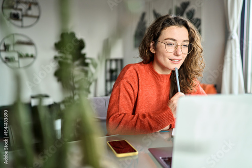 Online learning concept. Young smiling pretty woman student using laptop elearning or remote working at home office using laptop computer watching webinar web course, studying online sitting at table.