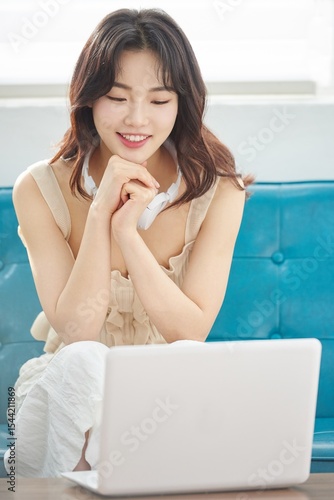 Young Asian Woman Relaxing on Sofa with Headphones and Laptop in Bright Living Room Free Download Young Asian Woman Relaxing on Sofa with Headphones and Laptop in Bright Living Room - GFXLoad