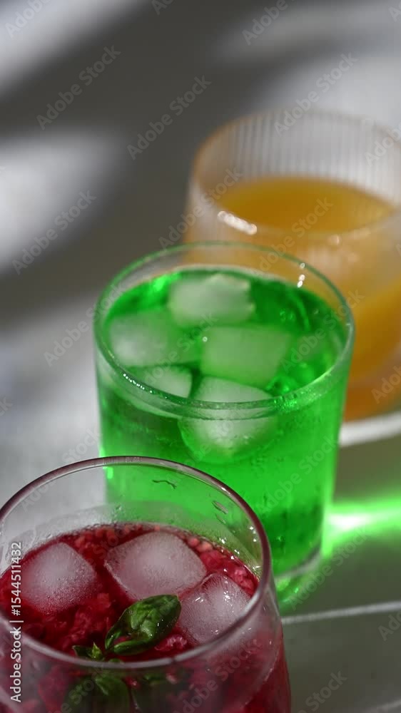 Three glass tumblers with red, yellow, and green lemonade on white background. Cold summer drinks with ice and condensation drops on glass surface. Refreshing for hot weather and restaurant Three glass tumblers with red, yellow, and green lemonade on white background. Cold summer drinks with ice and condensation drops on glass surface. Refreshing for hot weather and restaurant