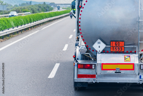 Rear view of a hazardous materials tanker truck, featuring the orange panel with hazard identification number and UN number, and a toxic liquid warning label.