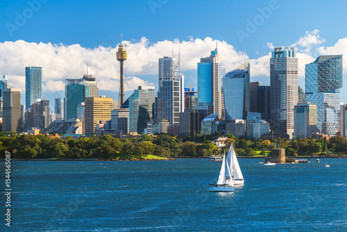 Beautiful Sydney city skyline panorama with tower and modern skyscrapers viewed across the harbour from Bradleys Head with blue sky and white fluffy clouds on a day