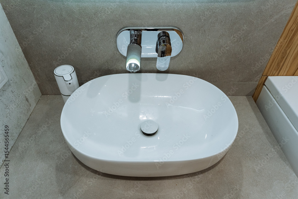 Fototapeta premium A white sink is placed in a bathroom, featuring a sleek faucet attached to it, making it both a functional plumbing fixture and an essential part of the bathrooms interior design