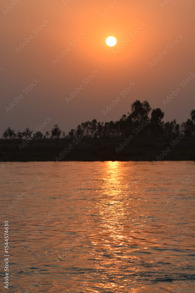 Naklejka premium Sindh Of Autumn River Landscape Or asia Part Of Pakista At Sunset. Sun Shine Over Blue Water Lake Or River At Sunrise. Nature At Sunny Morning. Woods With Orange Foliage On Riverside